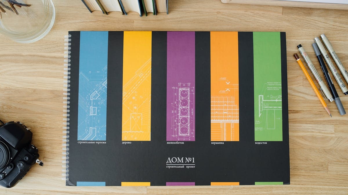 Design and architecture workbook with colorful blueprints on a wooden desk.